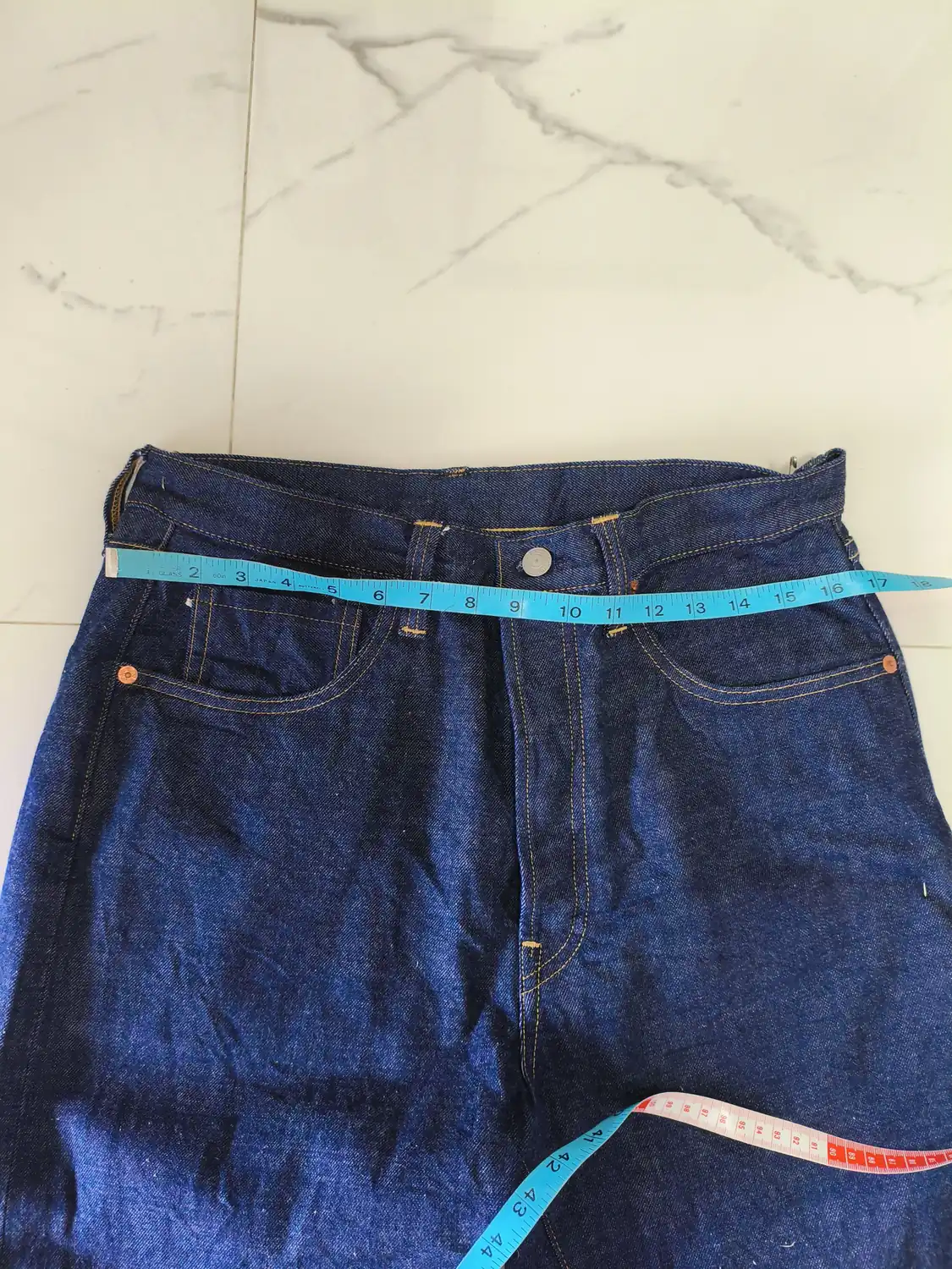 Indigo jeans measured across the waistband with a tape measure before alteration