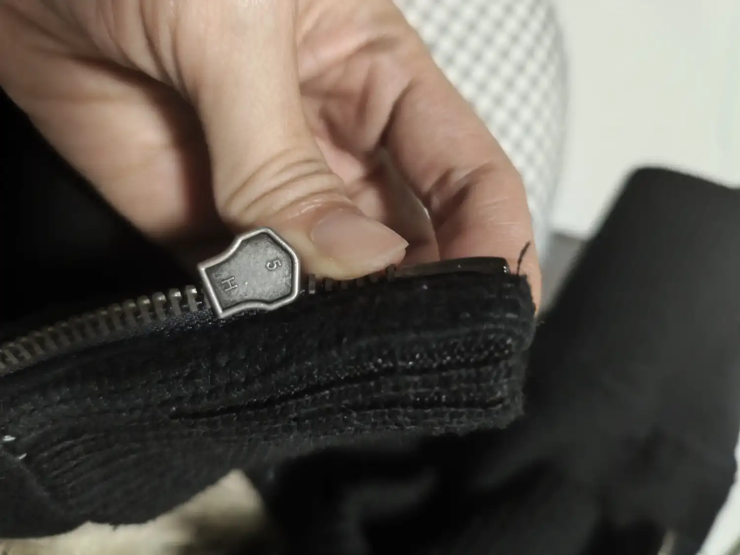 Hand working the pull of a metal zipper on a black knit garment