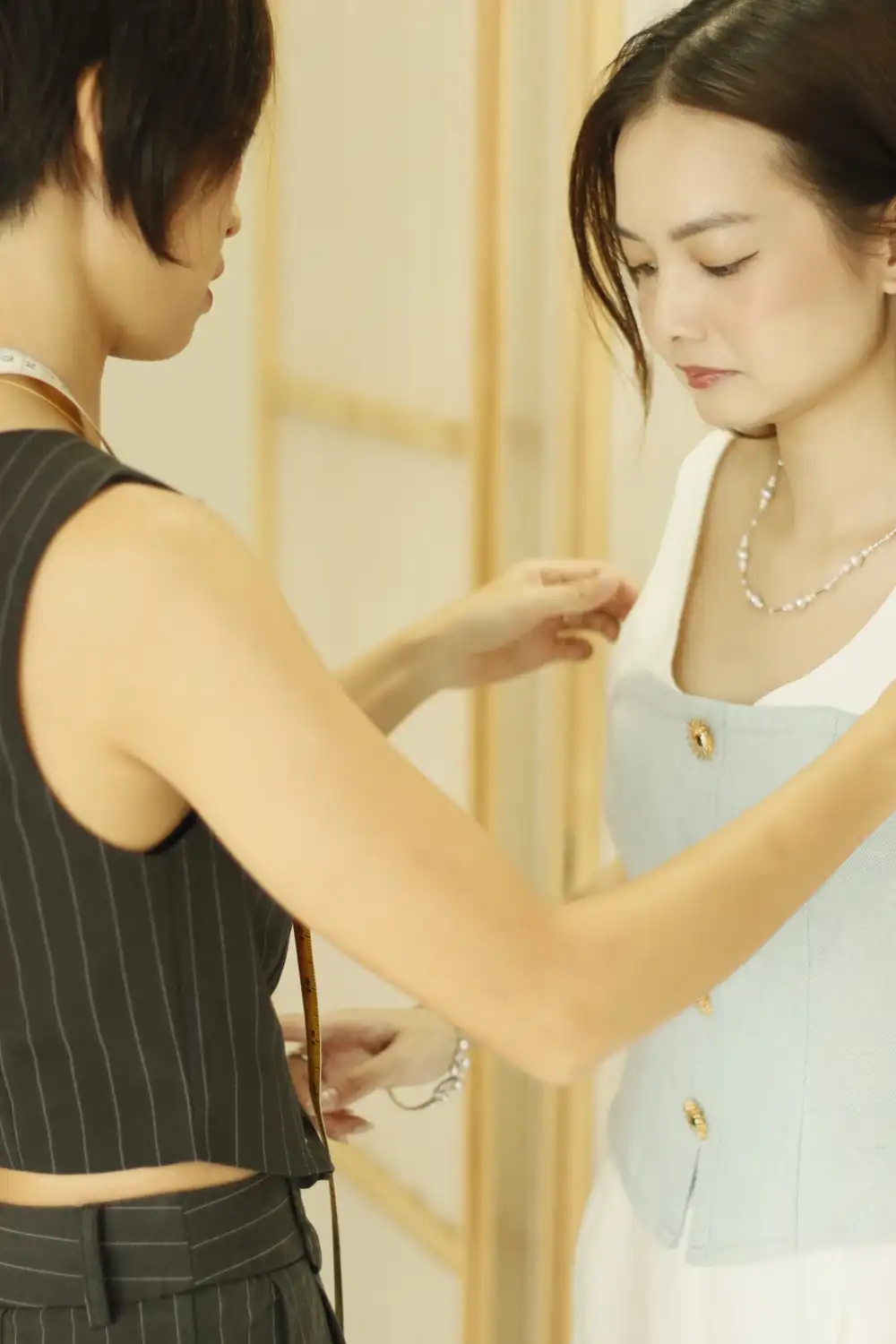 Seamstress pinning the fit of a client's top at the shoulder