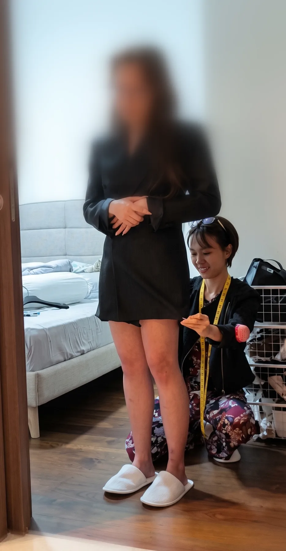 Hui Ling kneeling with a measuring tape, fitting a client's blazer dress at home in Singapore
